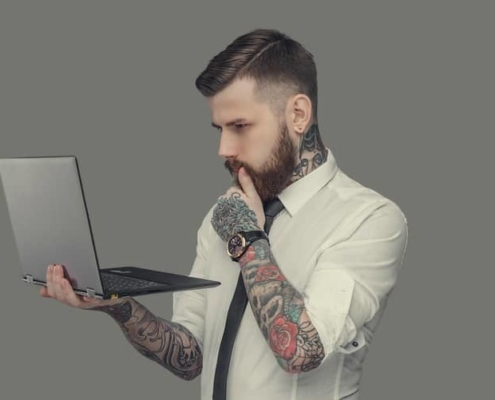 Bearded man in white shirt holding laptop. Isolated on grey background.