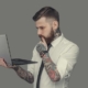 Bearded man in white shirt holding laptop. Isolated on grey background.